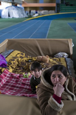 A woman sitting in a cardboard makeshift bed with a child behind her.